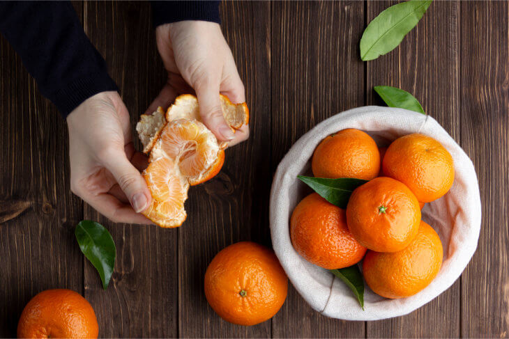 Mesa con bol de mandarinas y manos de mujer pelando una mandarina